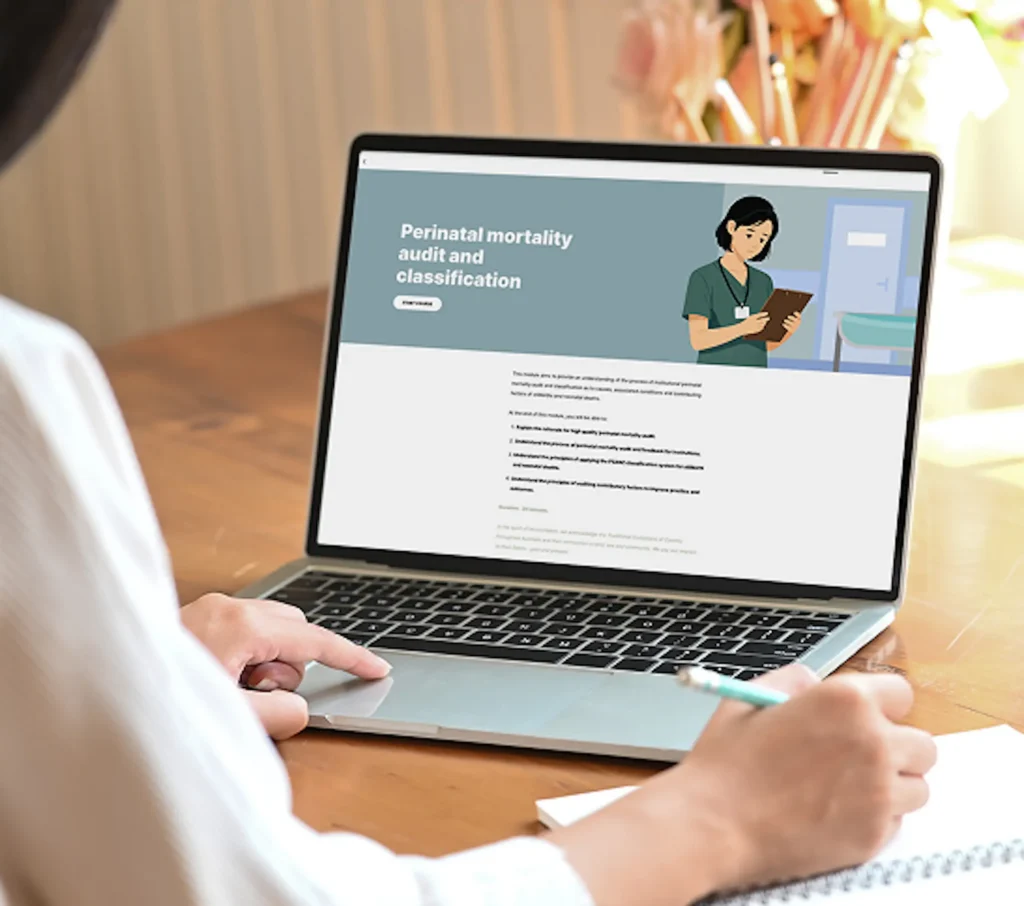 The image shows a person using a laptop displaying a webpage titled "Perinatal mortality audit and classification." The page features an illustration of a healthcare professional holding a clipboard. Below the title, there is a section of text providing information about perinatal mortality audits and classifications. The person is also holding a pen and writing in a notebook on the table beside the laptop.